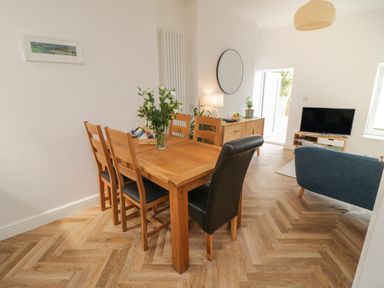A dining area with a wooden table and chairs next to a living space with a blue sofa and television at Through The Porthole in Falmouth