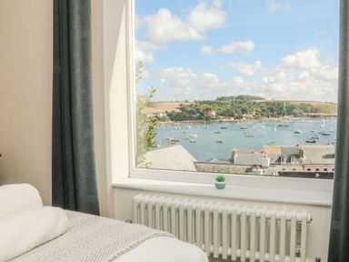 A bedroom window with a view of boats on water and hills at Through The Porthole in Falmouth
