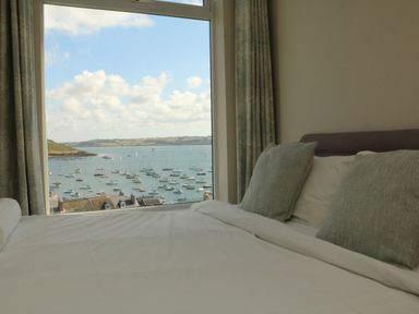 A bedroom with a bed and pillows facing a window with a view of boats on water at Through The Porthole in Falmouth