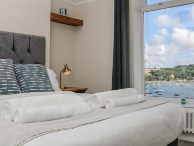 A bedroom with a bed with pillows and rolled towels next to a window overlooking a marina at Through The Porthole in Falmouth