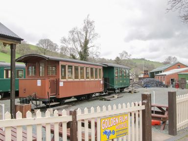 A vintage train carriage at a railway station with hills in the background at The Rhiw in Llanfair Caereinion