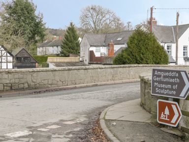 A street view with stone walls houses and signs pointing to Museum of Sculpture and a picnic area at The Rhiw in Llanfair Caereinion
