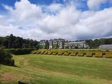 A large Tudor-style building with manicured hedges and a lawn under a partly cloudy sky at The Rhiw in Llanfair Caereinion