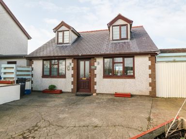 Front view of a two-story house with dormer windows and a paved driveway at Rhiangwyn Cottage in Llanrhyddlad near Cemaes Bay