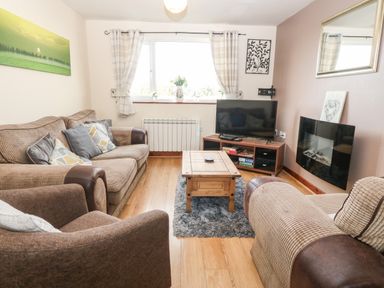 A living room with sofas a wooden coffee table a television and a wall-mounted electric fireplace at Rhiangwyn Cottage in Llanrhyddlad near Cemaes Bay