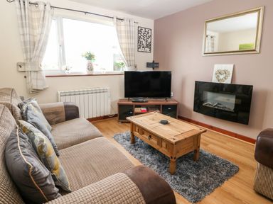 A living room with a sofa wooden coffee table flat screen tv and electric fireplace at Rhiangwyn Cottage in Llanrhyddlad near Cemaes Bay