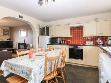 A kitchen with dining table and wooden chairs next to a living room at Rhiangwyn Cottage in Llanrhyddlad near Cemaes Bay