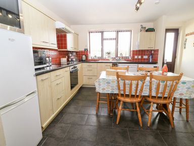 A kitchen with wooden cabinets a dining table with chairs and a refrigerator at Rhiangwyn Cottage in Llanrhyddlad near Cemaes Bay