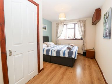 A bedroom with a bed striped bedspread window with curtains and wooden floor at Rhiangwyn Cottage in Llanrhyddlad near Cemaes Bay