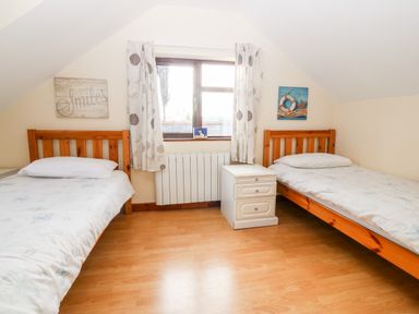 A bedroom with two single beds separated by a white nightstand and a window with curtains at Rhiangwyn Cottage in Llanrhyddlad near Cemaes Bay