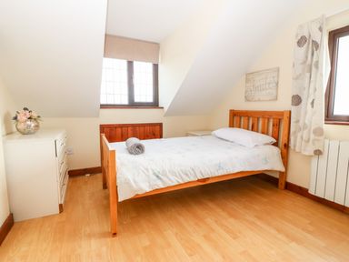 A bedroom with a wooden bed with white bedding a white dresser with flowers on top and two windows at Rhiangwyn Cottage in Llanrhyddlad near Cemaes Bay