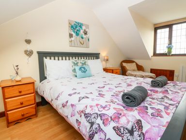 A bedroom with a bed with butterfly bedding two rolled towels bedside tables and a window with a chair at Rhiangwyn Cottage in Llanrhyddlad near Cemaes Bay