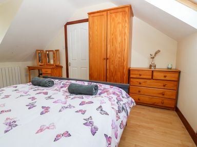 A bedroom with a bed covered with butterfly patterned bedding two rolled towels wooden wardrobe dresser with a vase and candle and a dressing table with mirrors at Rhiangwyn Cottage in Llanrhyddlad near Cemaes Bay