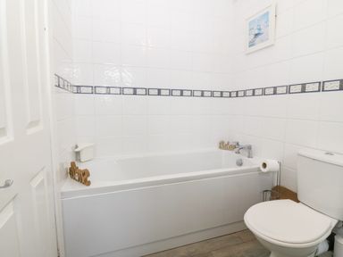 A bathroom with a bathtub a toilet and white tiled walls at Rhiangwyn Cottage in Llanrhyddlad near Cemaes Bay