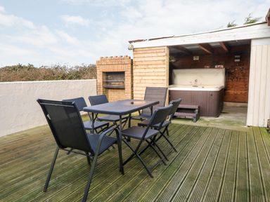 An outdoor deck with a dining table and six chairs a brick barbecue and a covered hot tub at Rhiangwyn Cottage in Llanrhyddlad near Cemaes Bay