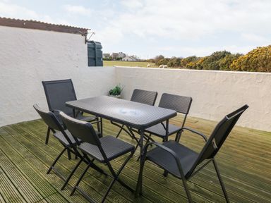 An outdoor patio with six black chairs and a black rectangular table at Rhiangwyn Cottage in Llanrhyddlad near Cemaes Bay