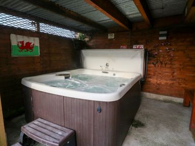 An indoor hot tub with bubbling water in a wooden shed with a Welsh flag on the wall at Rhiangwyn Cottage in Llanrhyddlad near Cemaes Bay