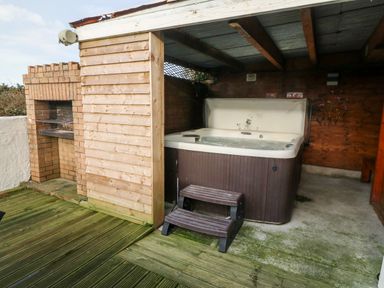 An outdoor covered patio with a hot tub a wooden step and a brick barbecue grill at Rhiangwyn Cottage in Llanrhyddlad near Cemaes Bay