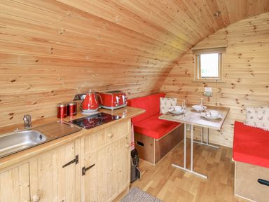 A small wooden kitchen and dining area with red cushions and appliances at Oak View in Llandovery