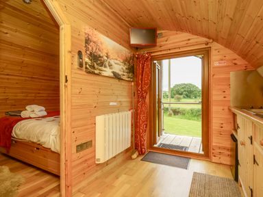 A small wooden cabin interior with a bed with towels a heating unit a wall-mounted TV and an open door leading to a grassy outdoor area at Oak View in Llandovery