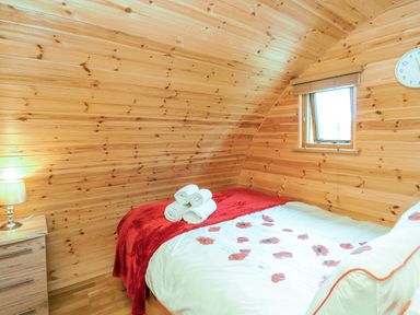 A bedroom with wooden walls a double bed with floral bedding a bedside table with a lamp and a wall clock at Oak View in Llandovery