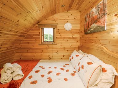 A bedroom with wood paneling a double bed with floral bedding and rolled towels on the bed at Oak View in Llandovery