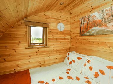 A wooden bedroom with a bed featuring floral bedding a small window a wall clock and a landscape painting at Oak View in Llandovery