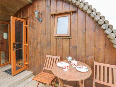 A wooden outdoor patio with a round table set with plates cups and a teapot at Oak View in Llandovery