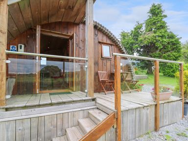 A wooden cabin porch with glass railing a table and two chairs surrounded by grass and trees at Oak View in Llandovery