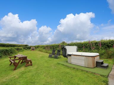An outdoor area with a wooden picnic table set two reclining chairs and a hot tub surrounded by hedges at Oak View in Llandovery