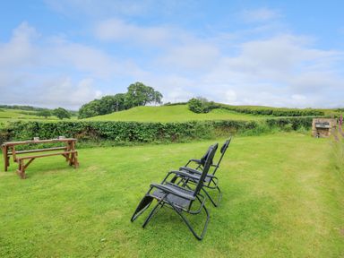 A grassy garden area with two black reclining chairs a wooden picnic table with cups and plates and a brick barbecue at Oak View in Llandovery