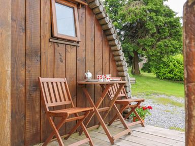 A small wooden table with two wooden chairs outside a wooden cabin with a window and flowers nearby at Oak View in Llandovery