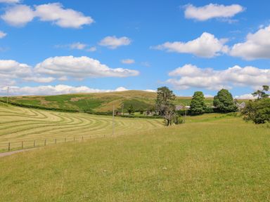 A landscape with grassy fields trees and houses under a blue sky at Oak View in Llandovery