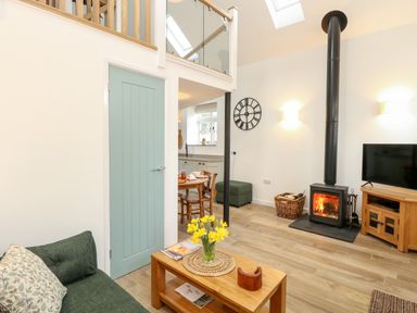 A living room with a green sofa wooden coffee table with flowers and a wood burning stove at Wensum Spring in Horningtoft near Fakenham
