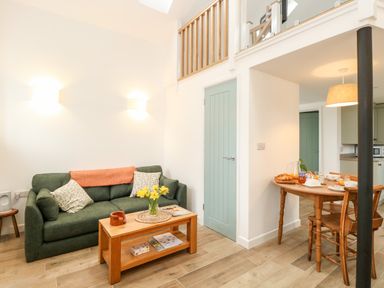 A living area with a green sofa and a wooden coffee table with flowers beside a dining table with chairs at Wensum Spring in Horningtoft near Fakenham