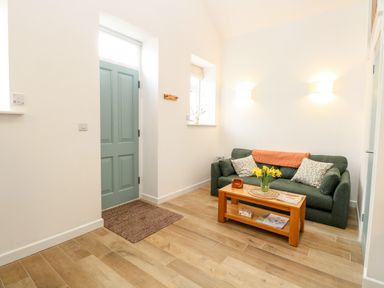A sitting area with a green sofa two cushions a wooden coffee table with flowers and magazines and a green door in Wensum Spring Horningtoft near Fakenham
