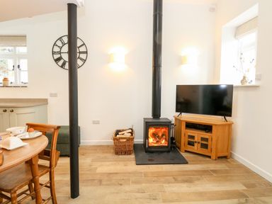 A living room with a wood-burning stove television on a stand wooden dining table and chairs at Wensum Spring in Horningtoft near Fakenham