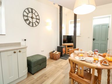 A dining area with a wooden table set for breakfast a wood stove and a wall clock at Wensum Spring in Horningtoft near Fakenham