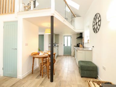 A kitchen and dining area with a wooden table and chairs a green door and cabinets a wall clock and a green ottoman at Wensum Spring in Horningtoft near Fakenham
