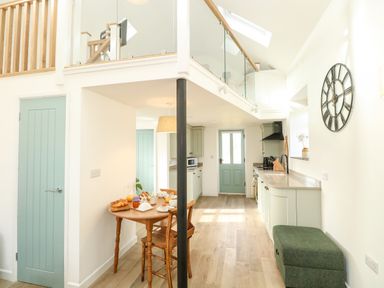 A kitchen and dining area with wooden table and chairs green doors and cabinets a clock on the wall and a green bench at Wensum Spring in Horningtoft near Fakenham