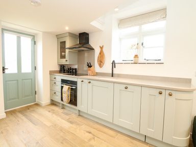 A kitchen with light green cabinets wooden floor and a window at Wensum Spring in Horningtoft near Fakenham