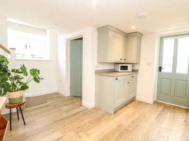 A kitchen area with wooden floor a built in cabinet with microwave and two doors at Wensum Spring Horningtoft near Fakenham