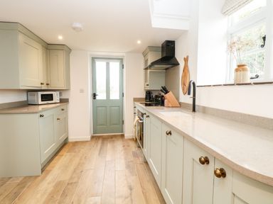 A kitchen with wooden floor cabinets a microwave a knife block and a window at Wensum Spring Horningtoft near Fakenham