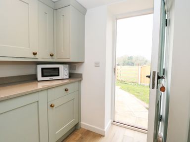 A kitchen corner with cabinets a microwave and an open door leading outside at Wensum Spring in Horningtoft near Fakenham