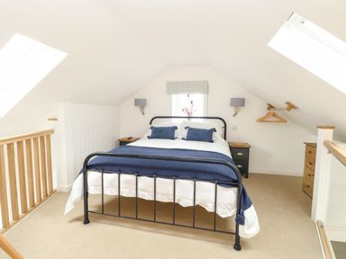 A bedroom with a double bed with blue pillows and blanket two bedside tables and skylights at Wensum Spring in Horningtoft near Fakenham