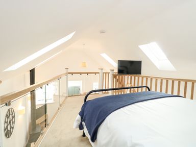 A loft bedroom with a bed a television skylights and wooden railings at Wensum Spring in Horningtoft near Fakenham