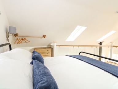A bedroom with a bed featuring blue pillows and blanket a wooden chest of drawers and hangers on a rack at Wensum Spring Horningtoft near Fakenham