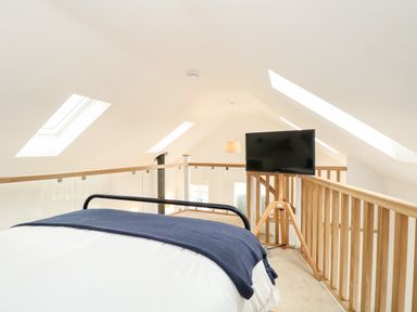 A loft bedroom with a bed covered with a blanket and a television mounted on a wooden stand at Wensum Spring in Horningtoft near Fakenham
