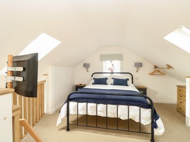 A bedroom with a metal bed frame two pillows blue blanket window and television at Wensum Spring in Horningtoft near Fakenham