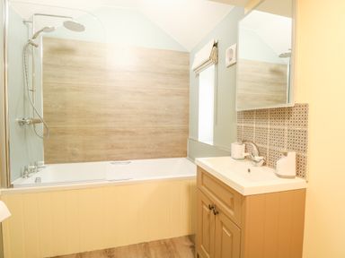 A bathroom with a bathtub shower, wooden paneling, sink with cabinet and a patterned tile backsplash at Wensum Spring in Horningtoft near Fakenham